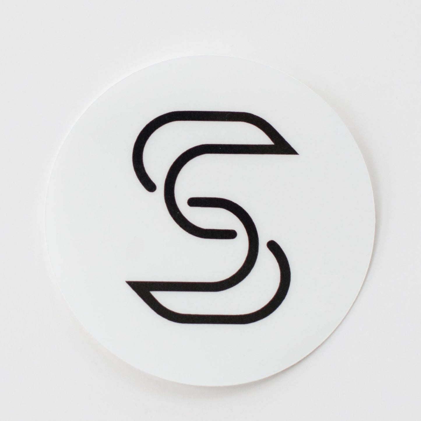 A circular, clear sticker of a black Stickr logo in front of a white background