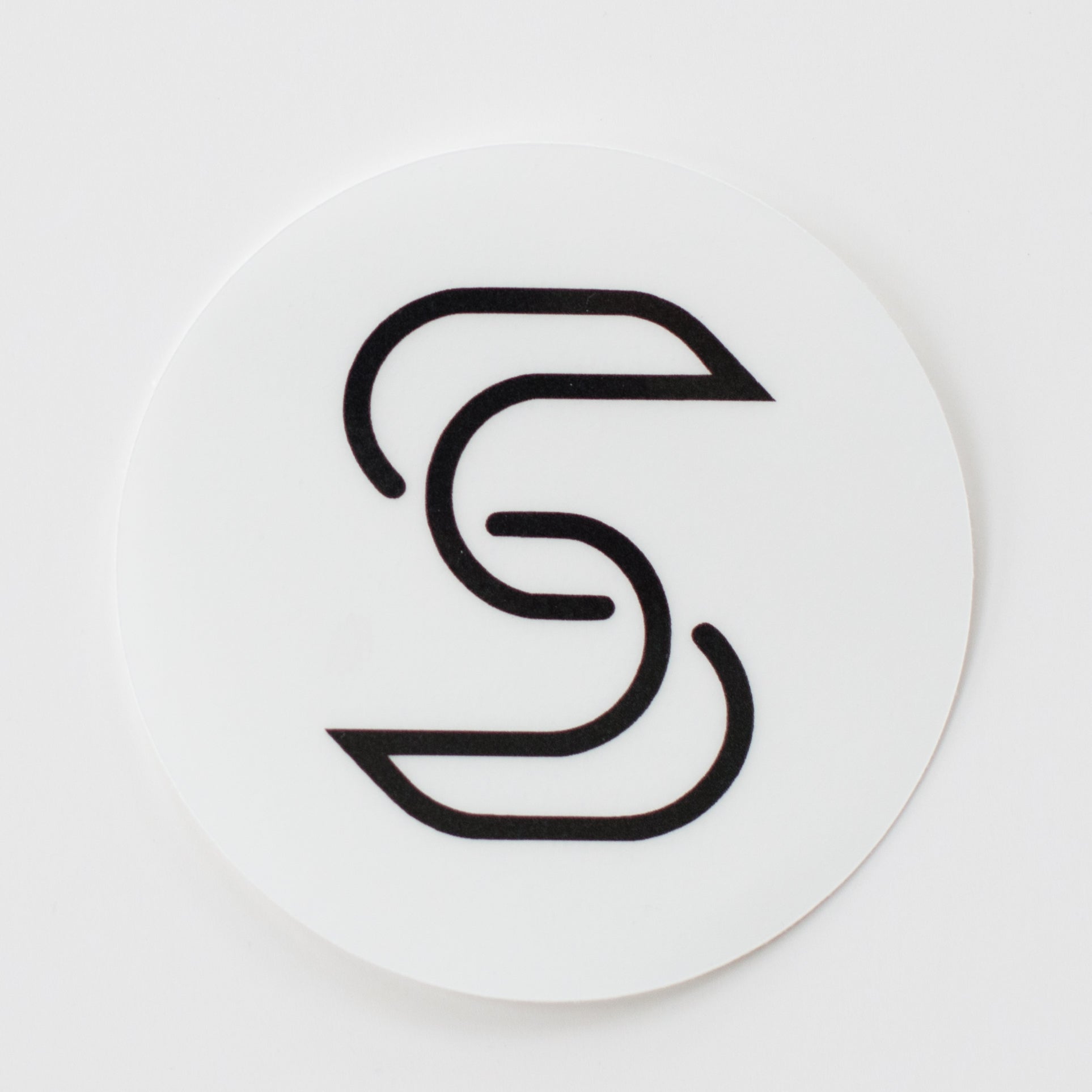 A circular, clear sticker of a black Stickr logo in front of a white background
