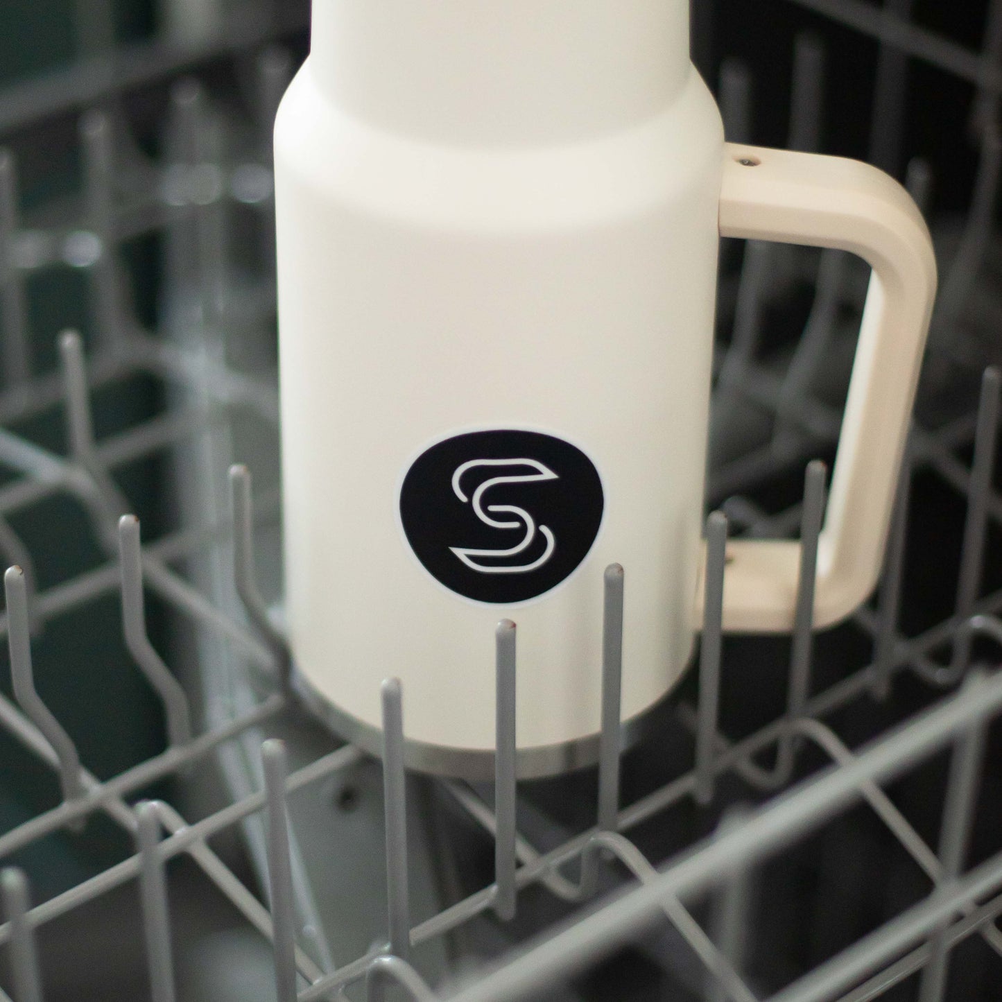 A circular black vinyl sticker of the Stickr logo on a water bottle in a dishwasher