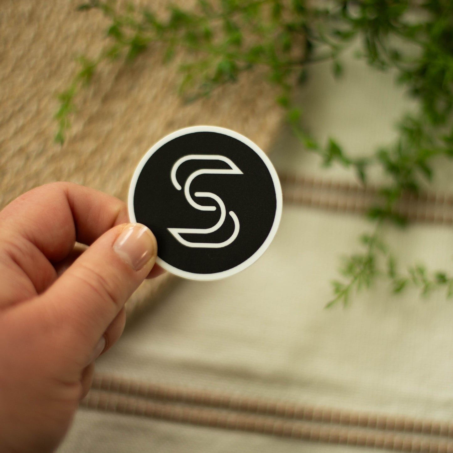 A hand holding a circular vinyl sticker of the Stickr logo