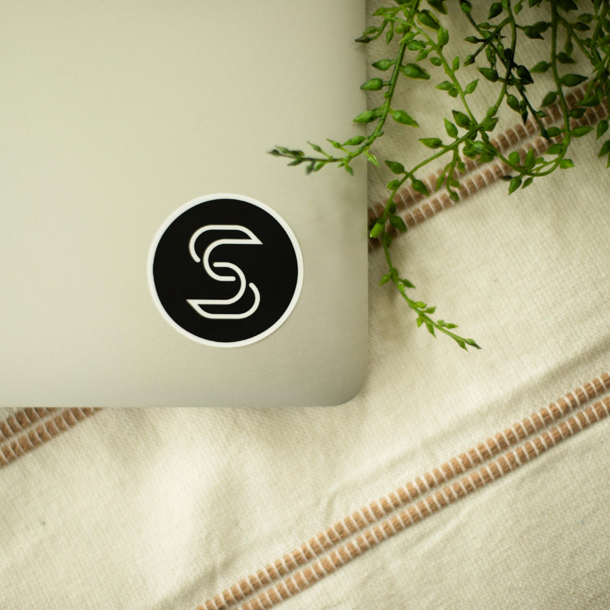 A circular vinyl sticker of the Stickr logo on a laptop