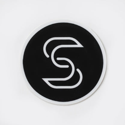 A black, circular sticker with a white Stickr logo is featured in front of a white background. 