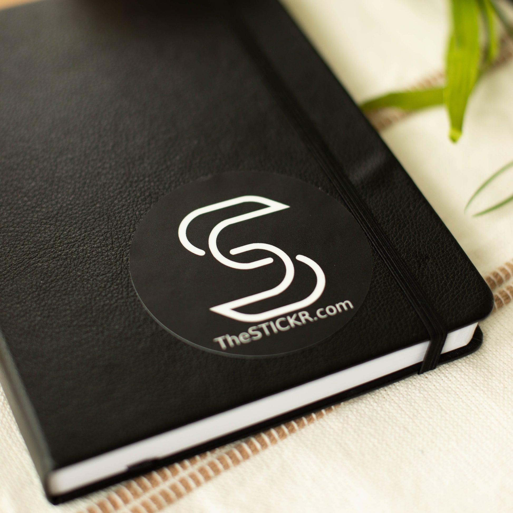 A black circular vinyl sticker of the Stickr logo and website on a notebook