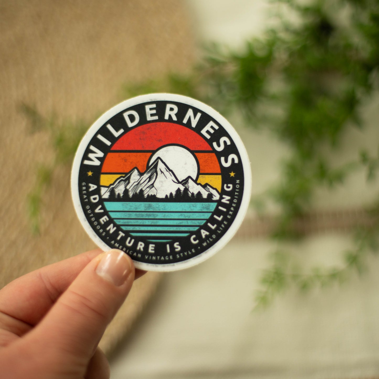 A hand holding a circular, vinyl sticker of a colorful mountain landscape