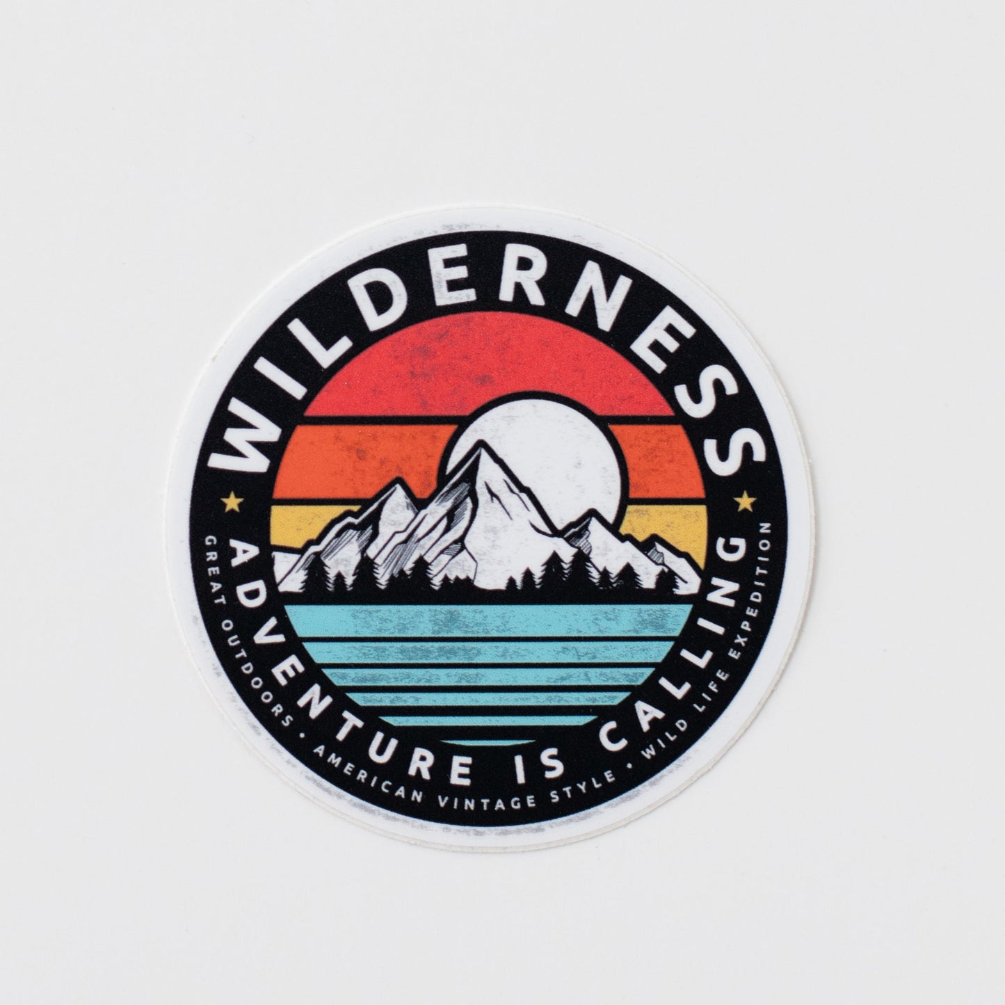A circular, vinyl sticker of a colorful mountain landscape in front of a white background