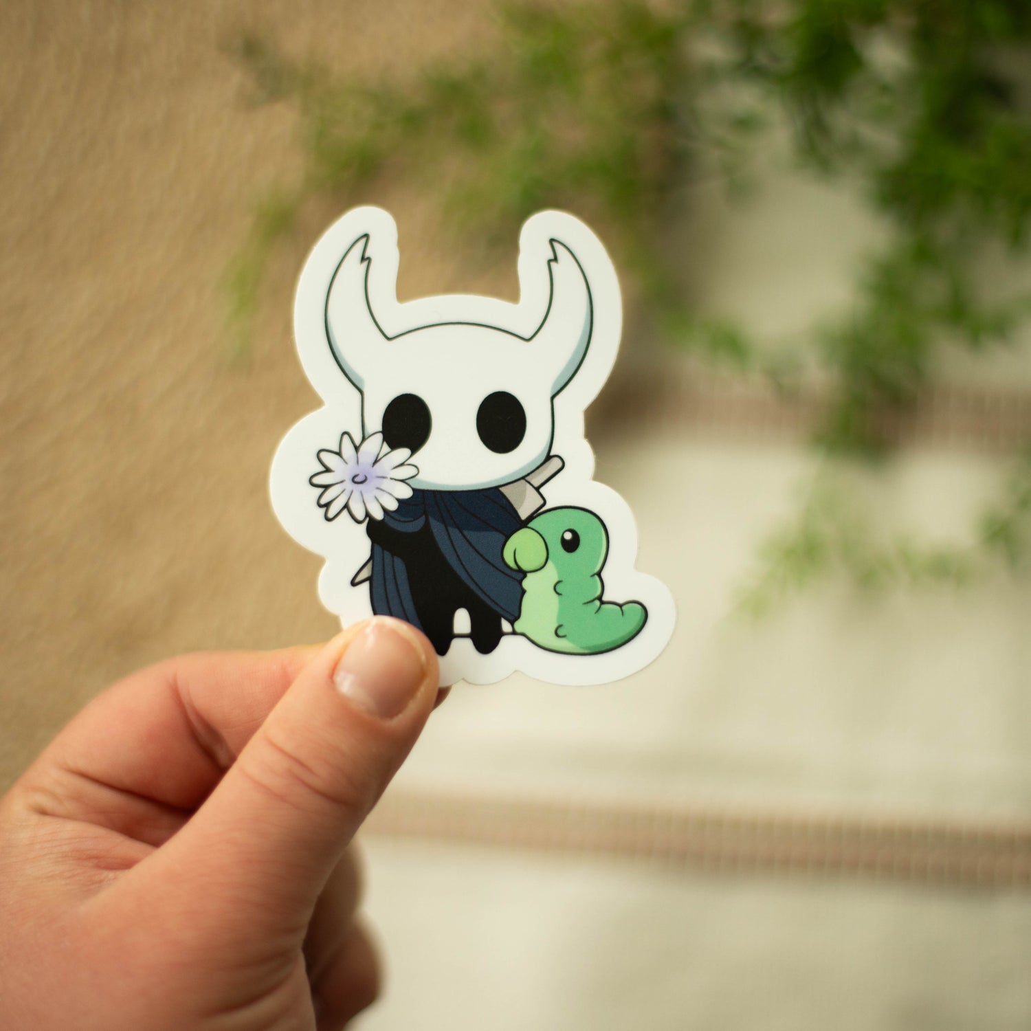 A hand holding vinyl sticker of Hallow Knight