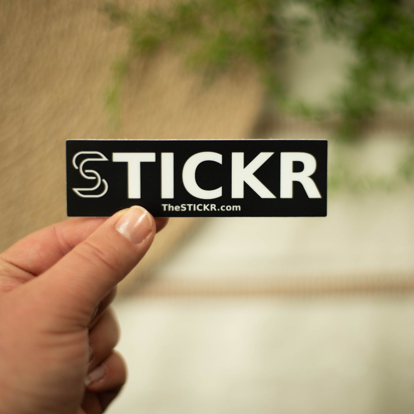 A hand holding a black rectangular shaped vinyl sticker of the Stickr logo and website