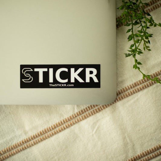 A rectangular black sticker of the Stickr logo and website on a laptop