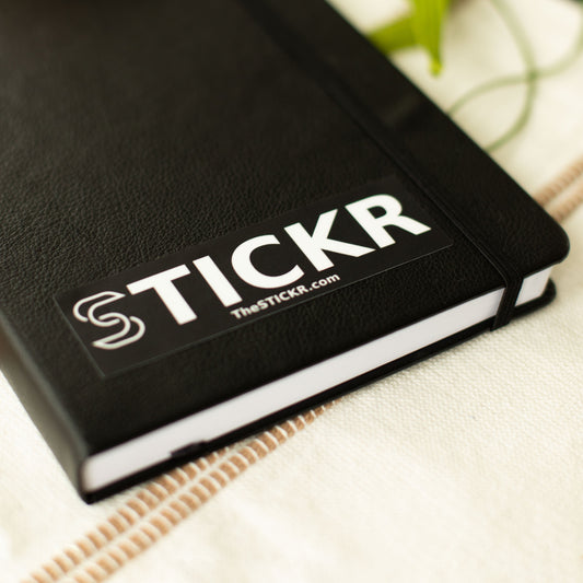A rectangular black sticker of the Stickr logo and website on a notebook