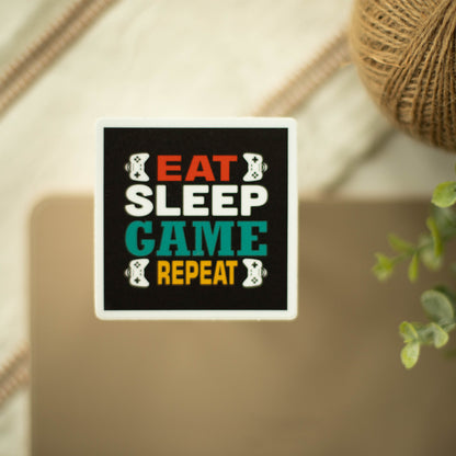 A square-shaped sticker with the words eat sleep game repeat and images of game controllers on a fancy background