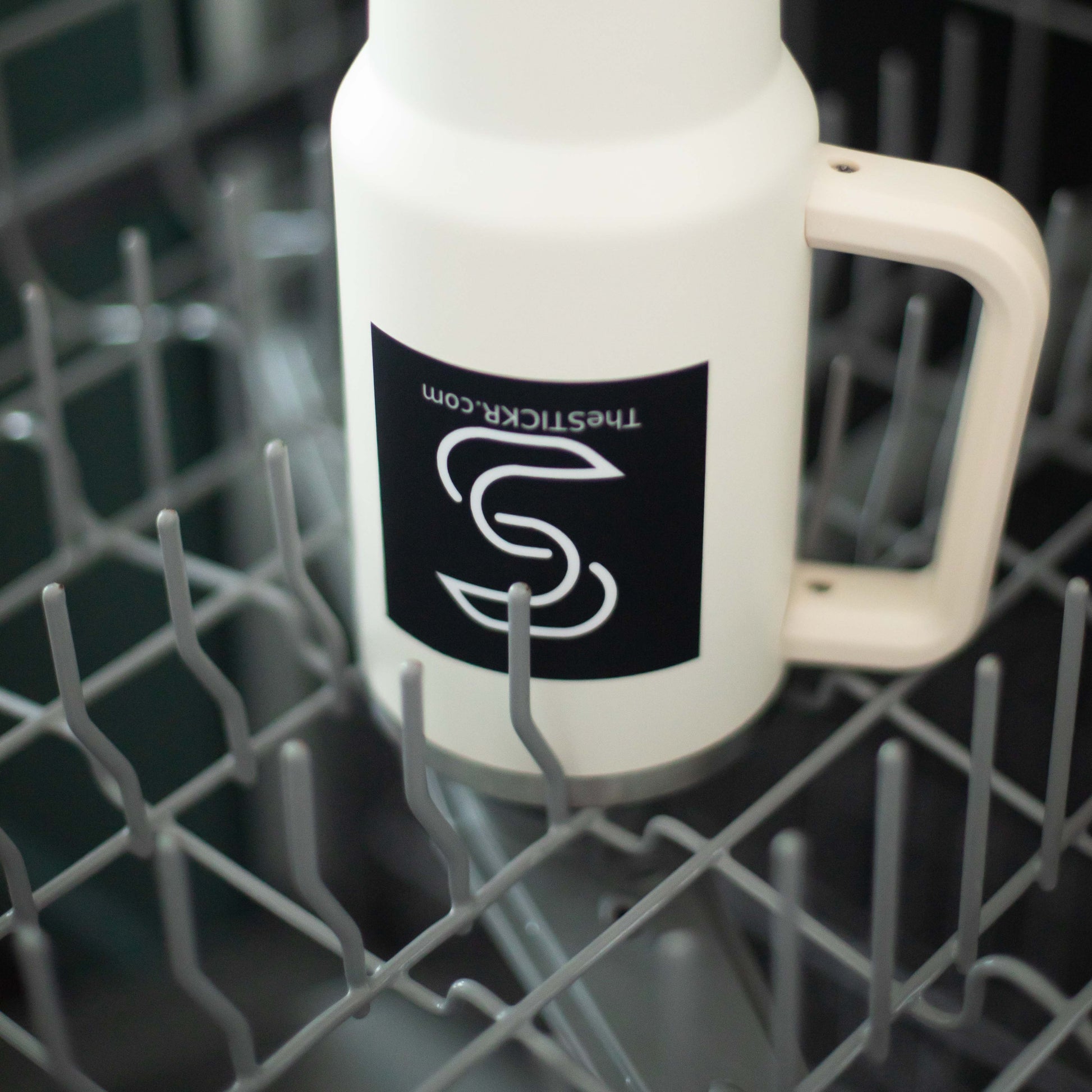 A square-shaped black vinyl sticker with the Stickr logo and website on a water bottle in a dishwasher