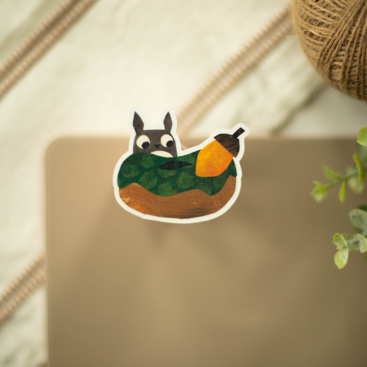 A clear sticker of a squirrel looking at an acorn on a fancy background