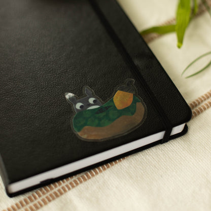 A clear sticker of a squirrel looking at an acorn on a notebook