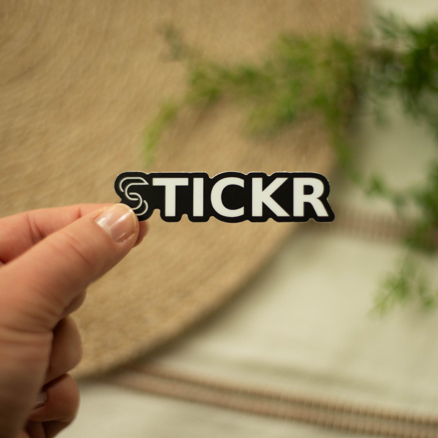 A hand holding a black and white vinyl sticker of the Stickr logo