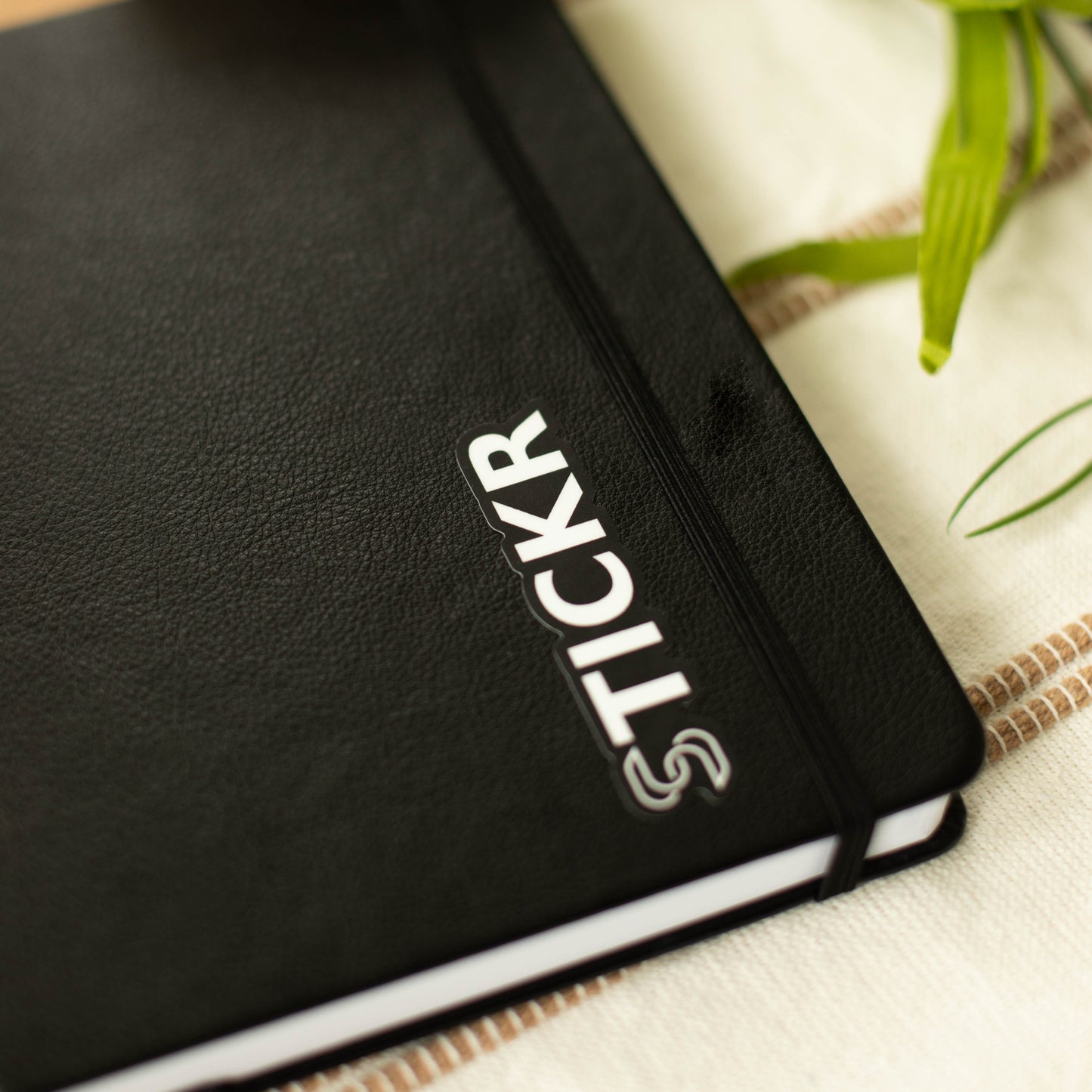A black and white vinyl sticker of the Stickr logo on a notebook